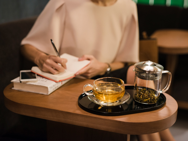 a woman writing on a notebook while having tea at The Pier, Cathay Pacific Business lounge