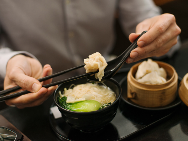 a close-up shot of a man eating noodles atThe Wing, Cathay Pacific Business lounge