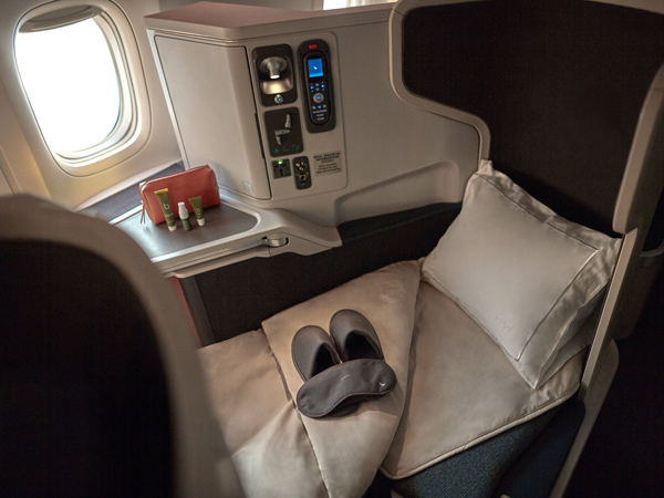 the window seat with a plush pillow, blanket, slipper and a mattress topper at Cathay Pacific Business Class