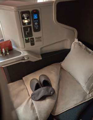 the window seat with a plush pillow, blanket, slipper and a mattress topper at Cathay Pacific Business Class