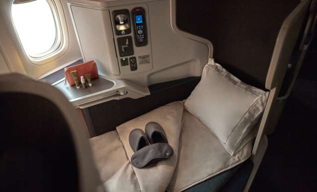 the window seat with a plush pillow, blanket, slipper and a mattress topper at Cathay Pacific Business Class
