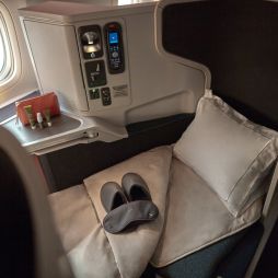 the window seat with a plush pillow, blanket, slipper and a mattress topper at Cathay Pacific Business Class
