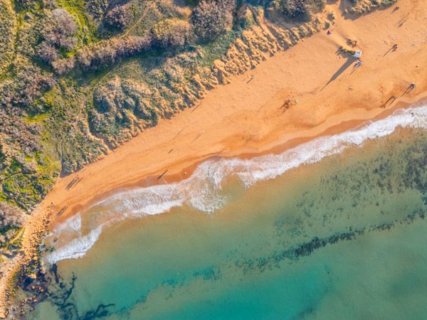 turquoise blue waters lapping against a golden sandy beach at Ramla Bay, Gozo, Malta