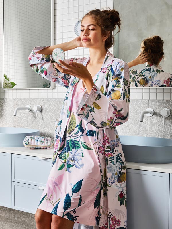 A woman wearing the robe in the bathroom while looking at herself in the mirror. 