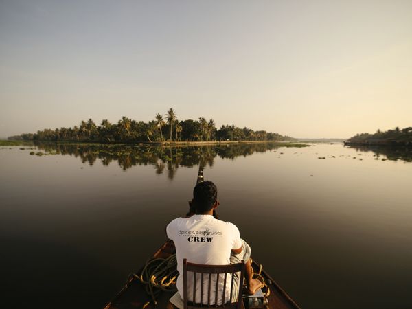 a boatman sitting at the edge of the Spice Coast Cruises houseboat on the river, Kerala Backwaters