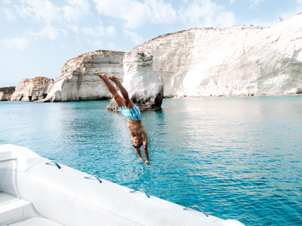 a man jumping into the Aegean sea in front of a volcanic rock