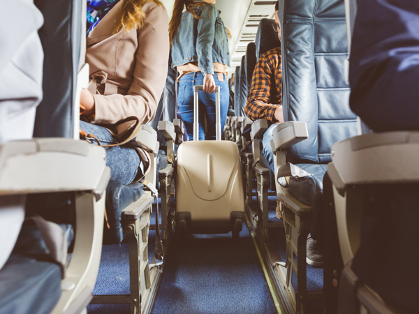 Interior of airplane with people sitting on seats. Passengers with suitcase in aisle looking for seat during flight.