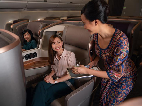 A Singapore airlines flight attendant offering a drink to the business class passenger.