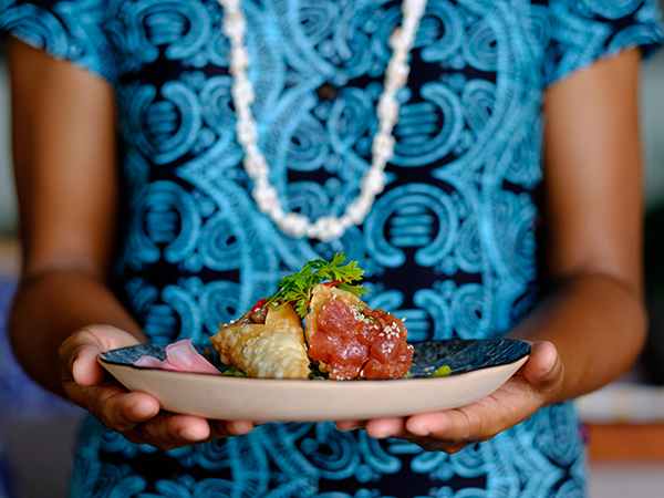 Hands gracefully offer a beautifully plated Pacific dish.