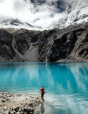 Person standing by the turquoise waters of Laguna 69 with glacier views.