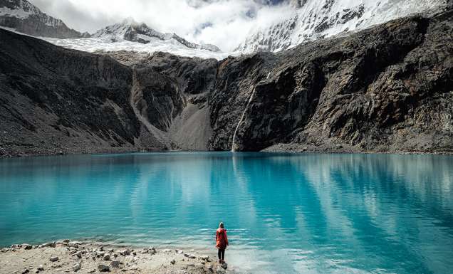 Person standing by the turquoise waters of Laguna 69 with glacier views.