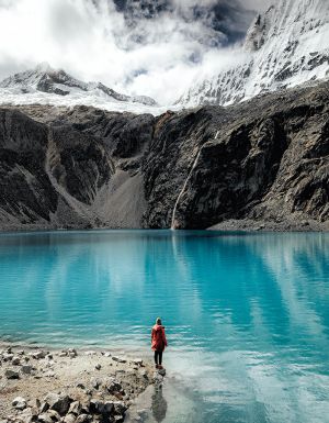 Person standing by the turquoise waters of Laguna 69 with glacier views.