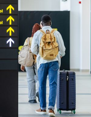 Groups of individuals walk towards passport control and customs at an airport, with signs showing directions, illustrating travel and passage through security processes.