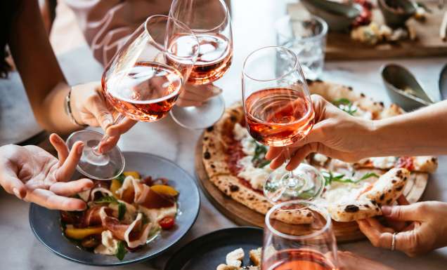 Friends enjoy a dinner party with pizza and rose wine in a bar or a restaurant.