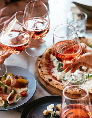 Friends enjoy a dinner party with pizza and rose wine in a bar or a restaurant.