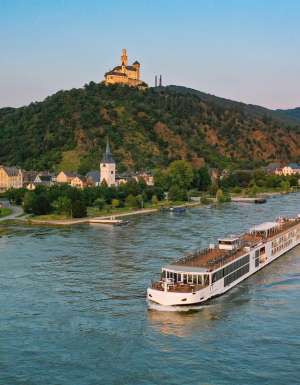Viking River Cruise ship, the Mimir, passing the historic Marksburg Castle near Braubach on the Rhine River at sunset.