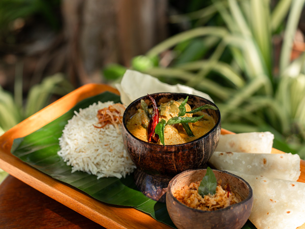 Maldivian Coconut Curry dish with tuna, jasmine rice and sambal chutney served in coconut shell and banana leaves