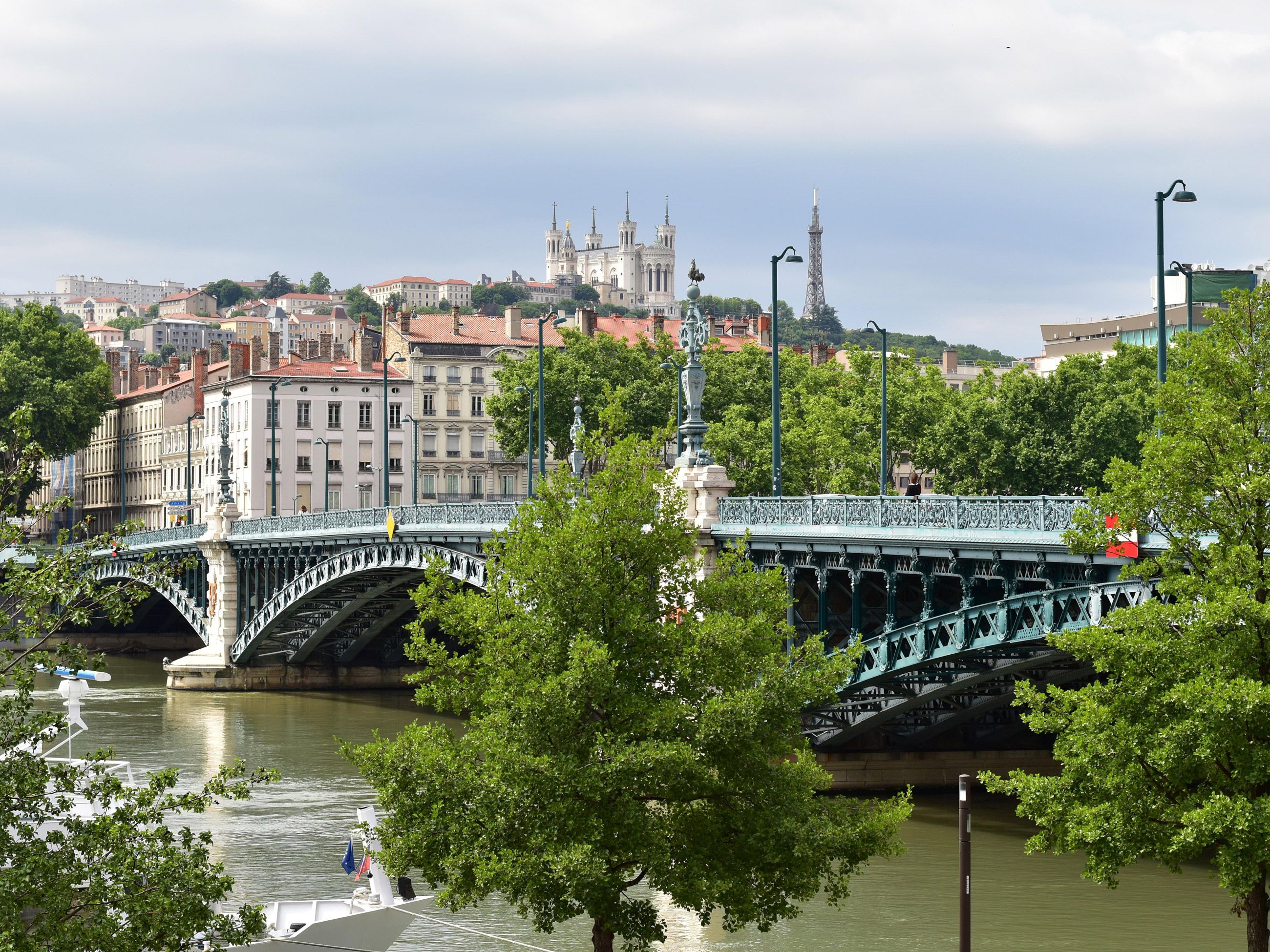 the historic Pont de l'Université crossing the Rhône River in Lyon, France, with the Basilica of Notre-Dame de Fourvière visible on the hill in the background